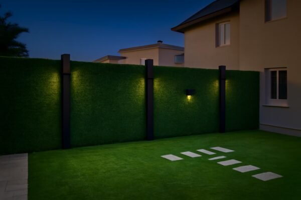 سياج أخضر صناعي مزين بأعمدة سوداء منيرة على خلفية منزل حديث وحديقة مزروعة بالعشب الصناعي